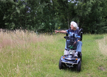 Foto: vrouw op scootmobiel wijst naar een plant in de berm